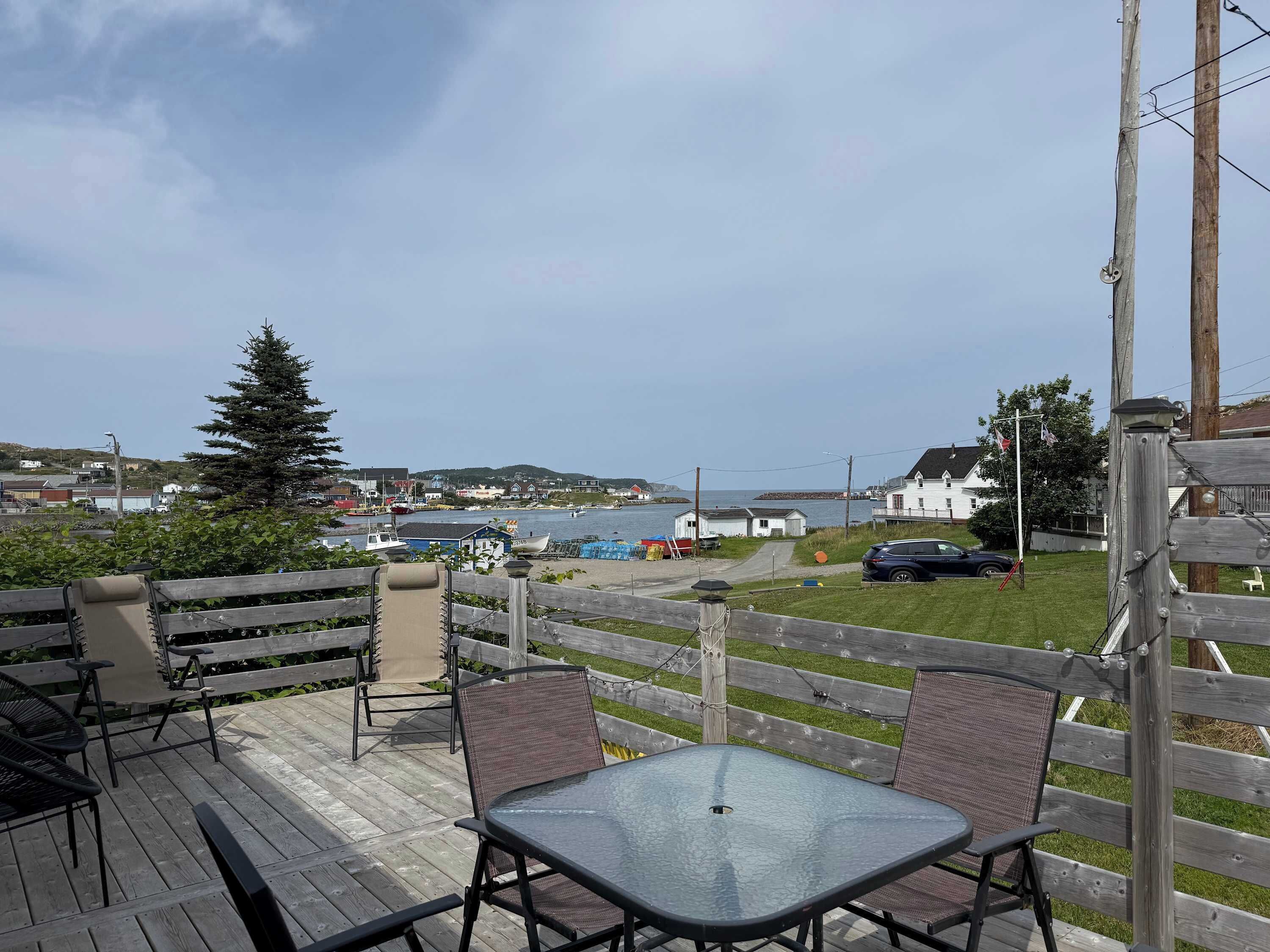 Een houten terras met buitenmeubilair, met uitzicht op een haven met boten en gebouwen.