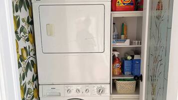 A compact laundry area with a washing machine and dryer, a shelf with cleaning supplies, and a patterned wall.