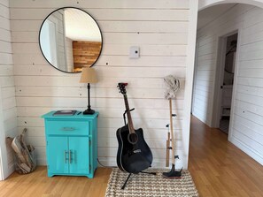 A room with a turquoise cabinet, a guitar, a mop, and a mirror on the wall. - The Shoal Tickle House (Twillingate)