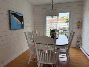 A dining area with a white table and chairs, a hanging light fixture, a painting of a whale, and a sign with rules.