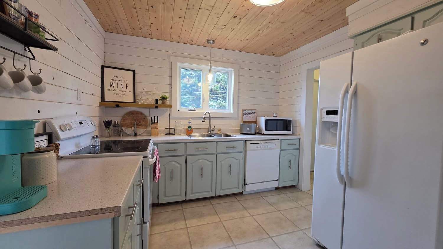 A kitchen with a wooden ceiling, white cabinets, a microwave, a refrigerator, and a window with natural light.