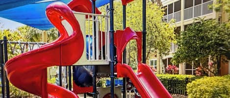 Une aire de jeux avec des toboggans rouges et une structure bleue en forme de tonnelle.