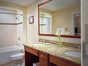Un baño con lavamanos doble, bañera, espejo y un cuadro en la pared.