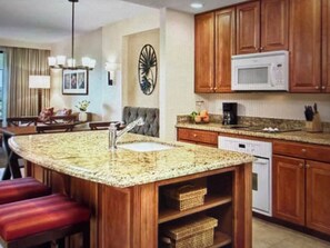 A kitchen with wooden cabinets, a granite countertop, a built-in microwave, and a coffee maker. - Cozy 1-bedroom condo near Disney in Orlando with pool and activities (Orlando)