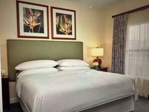 Una habitación de hotel con una cama, una mesita de noche, una lámpara y dos cuadros en la pared.