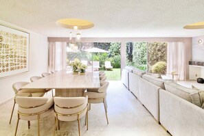 Uma sala de jantar moderna com uma mesa comprida e cadeiras, um sofá e vista para o jardim.