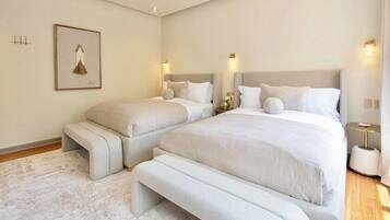 Quarto com duas camas, um banco e luminárias fixadas na parede.