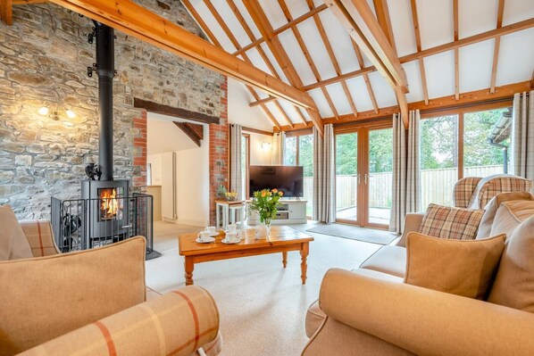 A cozy living room with a stone wall, a fireplace, a television, and comfortable seating. - 3 Bed in Kilkhampton (oc-l27383) (Kilkhampton)