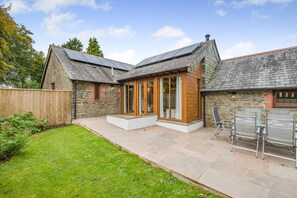 A stone house with a patio, a wooden deck, and a glass-enclosed dining area. - 3 Bed in Kilkhampton (oc-l27383) (Kilkhampton)