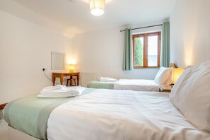 A hotel room with two beds, a table, a lamp, and a window with curtains. - 3 Bed in Kilkhampton (oc-l27383) (Kilkhampton)