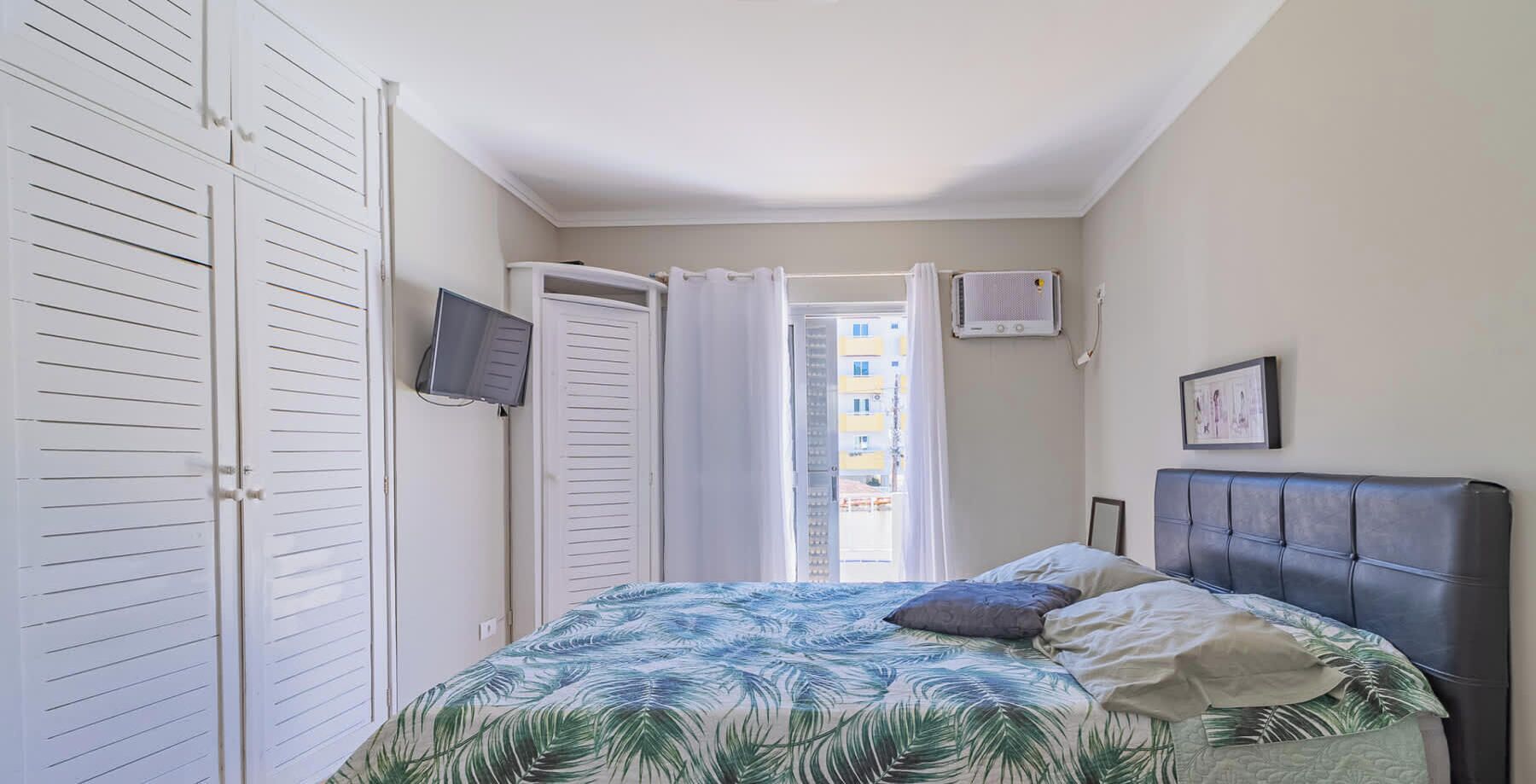Une chambre à coucher avec un lit, une télévision, une armoire et une fenêtre avec des rideaux.