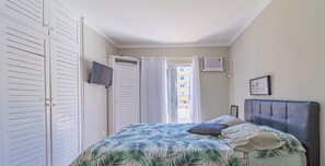 Ein Schlafzimmer mit Bett, Fernseher, Kleiderschrank und einem Fenster mit Vorhängen.