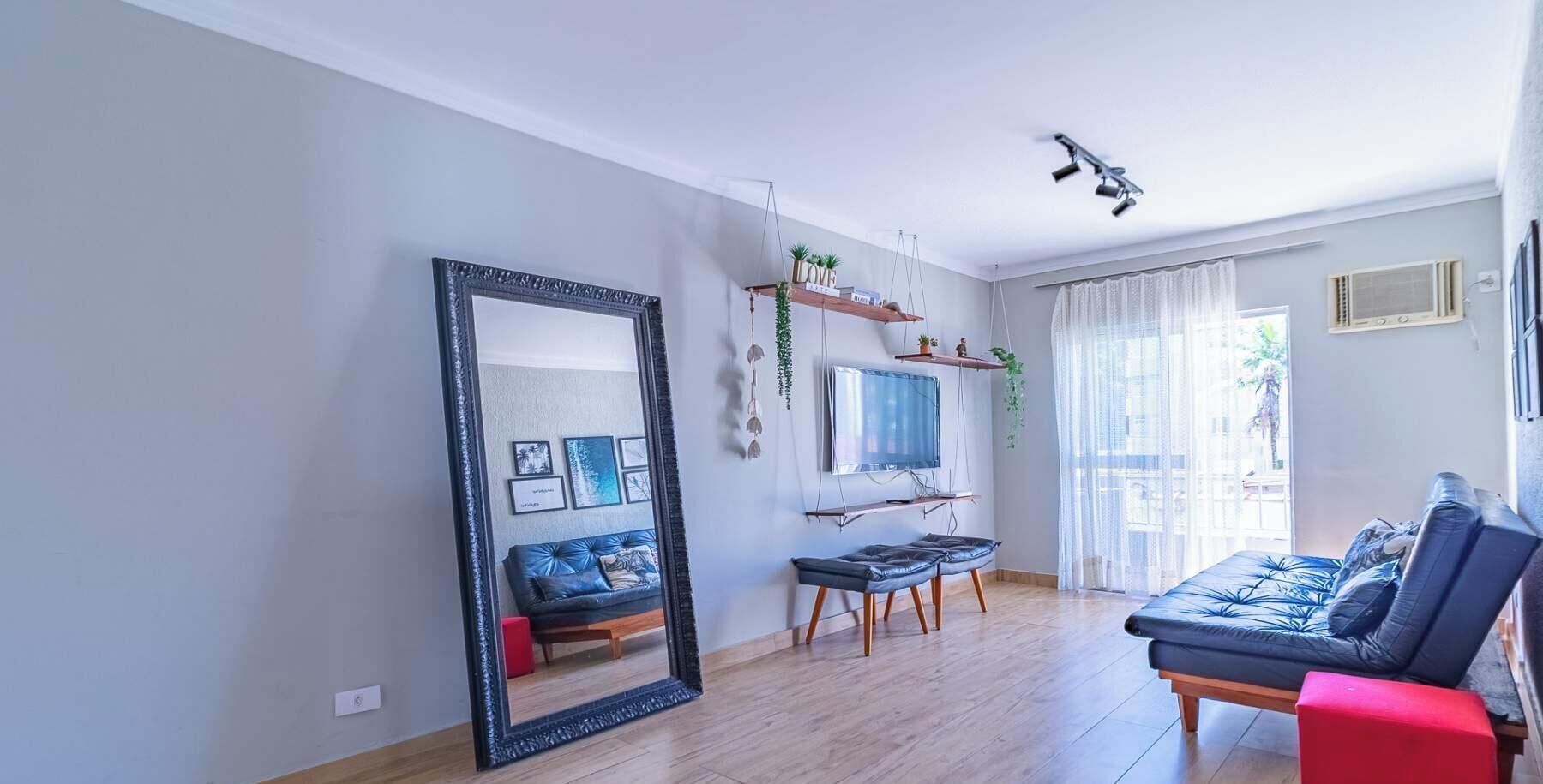 Un salon avec un grand miroir, un canapé, un téléviseur et une fenêtre avec des rideaux.