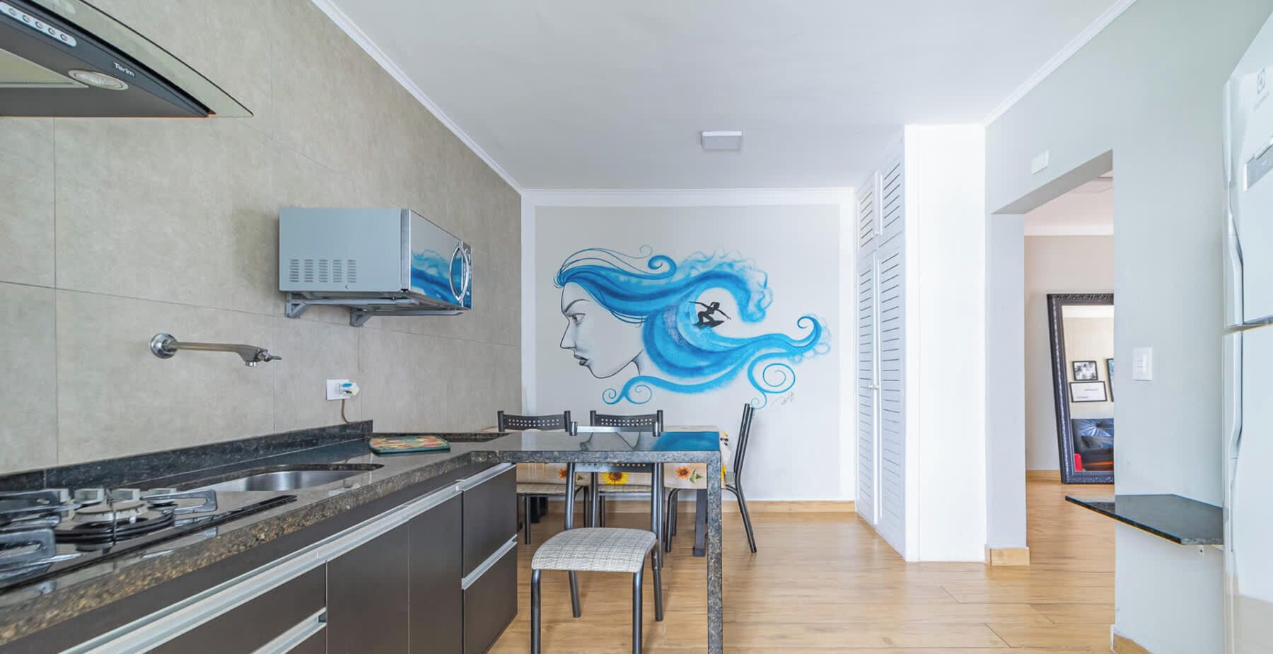 Une cuisine moderne dotée d’un four à micro-ondes encastré, d’un coin repas avec une table et des chaises, et d’une fresque murale.
