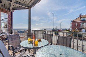 Ein Balkon mit Sitzgelegenheit im Freien, einem Tisch mit Frühstücksgebäck und Blick auf das Meer sowie einen Parkplatz.