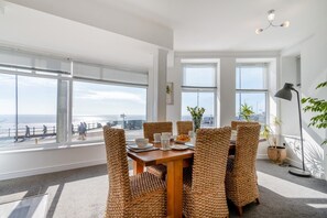Ein Essbereich mit Blick auf den Strand, mit Korbstühlen, einem Holztisch und einer Stehlampe.
