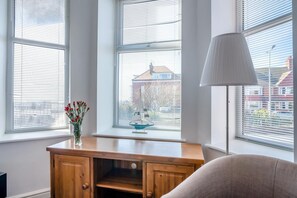 Ein Zimmer mit Schreibtisch aus Holz, einer Lampe und einem Fenster mit einem Modell eines Segelboots.