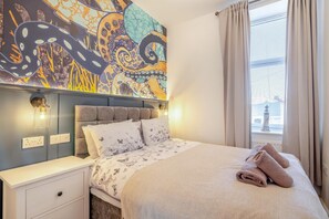 Ein Schlafzimmer mit Bett, Nachttischen, einer Wandmalerei und einem Fenster mit Vorhängen.