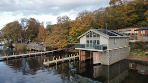 Ein Hausboot mit Glasbalkon, gelegen auf einem Gewässer mit einem Steg im Vordergrund.