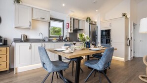 A modern kitchen with white cabinetry, a dining table with chairs, and a view of the outdoors through a window. - 2 Bed in Newby Bridge (oc-b30231) (Newby Bridge)