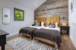 Ein Schlafzimmer mit zwei Betten, einem Fenster, einer Holzwand und einem schwarzen Nachttisch.