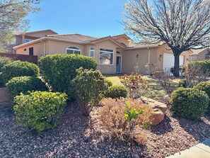 A residential house with a well-maintained garden, including various shrubs and a tree. - Comfort & Convenience close to Zion, Sand Hollow, Quail Creek & Gooseberry Mesa! (Hurricane)