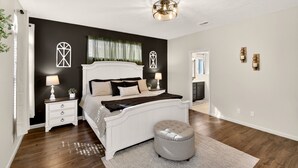 A bedroom with a large bed, bedside tables, a nightstand, a round ottoman, and a ceiling light fixture. - Comfort & Convenience close to Zion, Sand Hollow, Quail Creek & Gooseberry Mesa! (Hurricane)