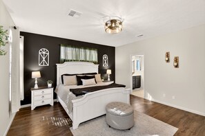 A bedroom with a large bed, bedside tables, a nightstand, a round ottoman, and a ceiling light fixture. - Comfort & Convenience close to Zion, Sand Hollow, Quail Creek & Gooseberry Mesa! (Hurricane)