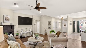 A spacious living room with a fireplace, a ceiling fan, a television, and a dining area with a view of the outside. - Comfort & Convenience close to Zion, Sand Hollow, Quail Creek & Gooseberry Mesa! (Hurricane)