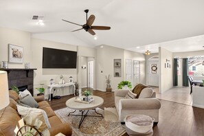 A spacious living room with a fireplace, a ceiling fan, a television, and a dining area with a view of the outside. - Comfort & Convenience close to Zion, Sand Hollow, Quail Creek & Gooseberry Mesa! (Hurricane)