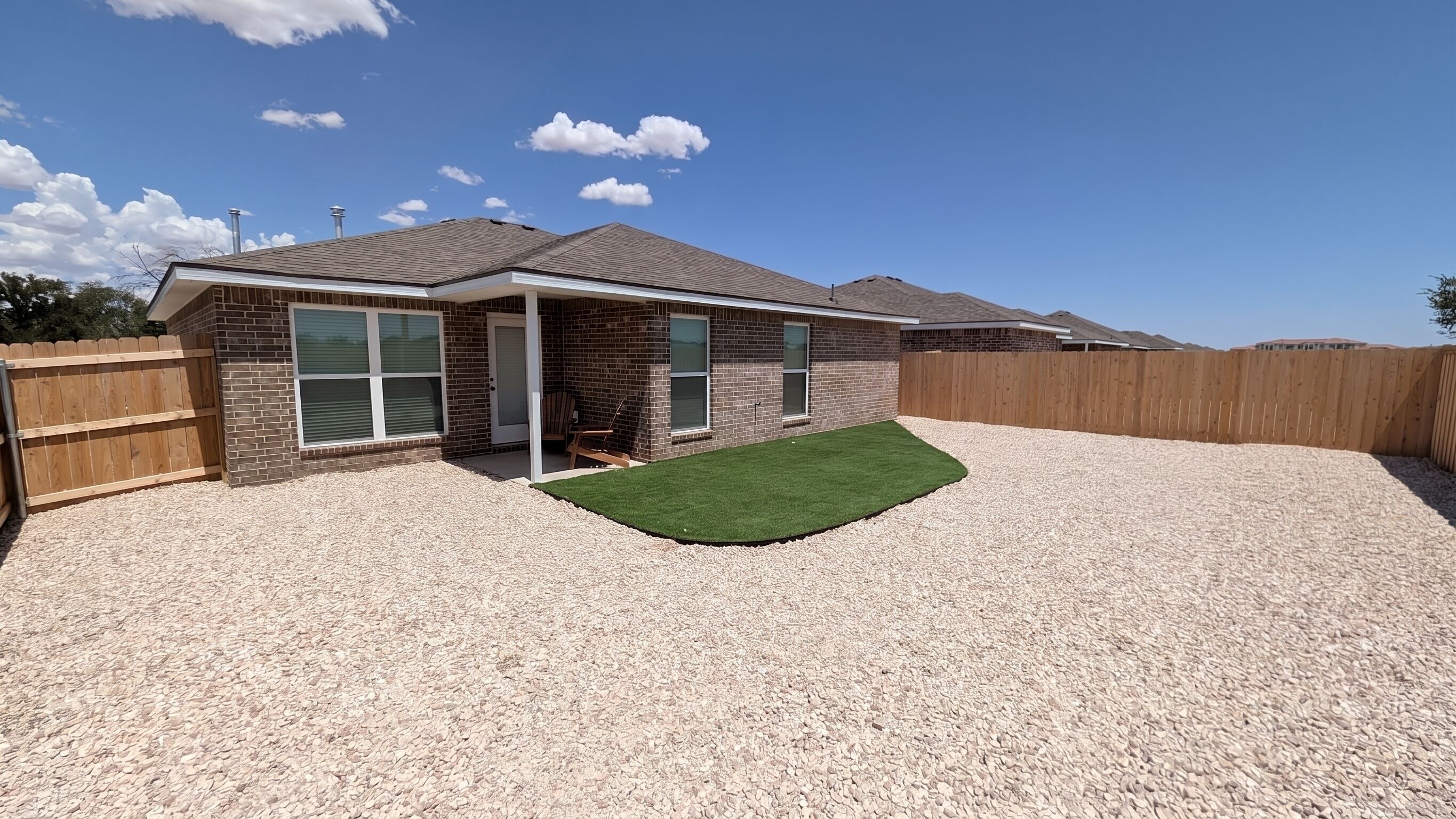 A residential house with a brick exterior, a covered patio, and a gravel driveway.