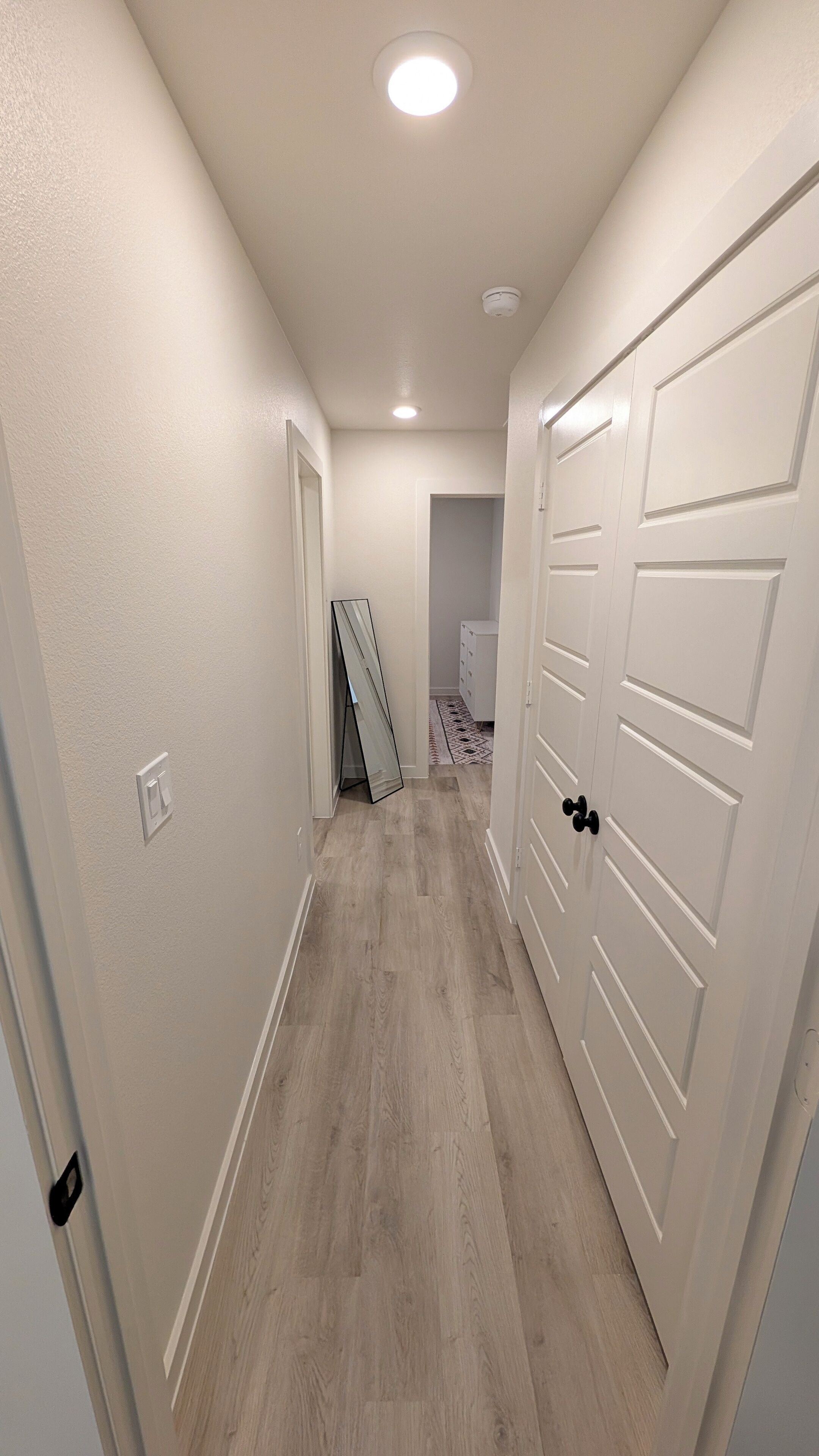 Un couloir doté d’un plancher en bois, de murs blancs et d’une porte avec une poignée noire.
