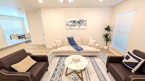Un salon avec un canapé beige, deux canapés en cuir marron, une table basse et un tapis à motifs.