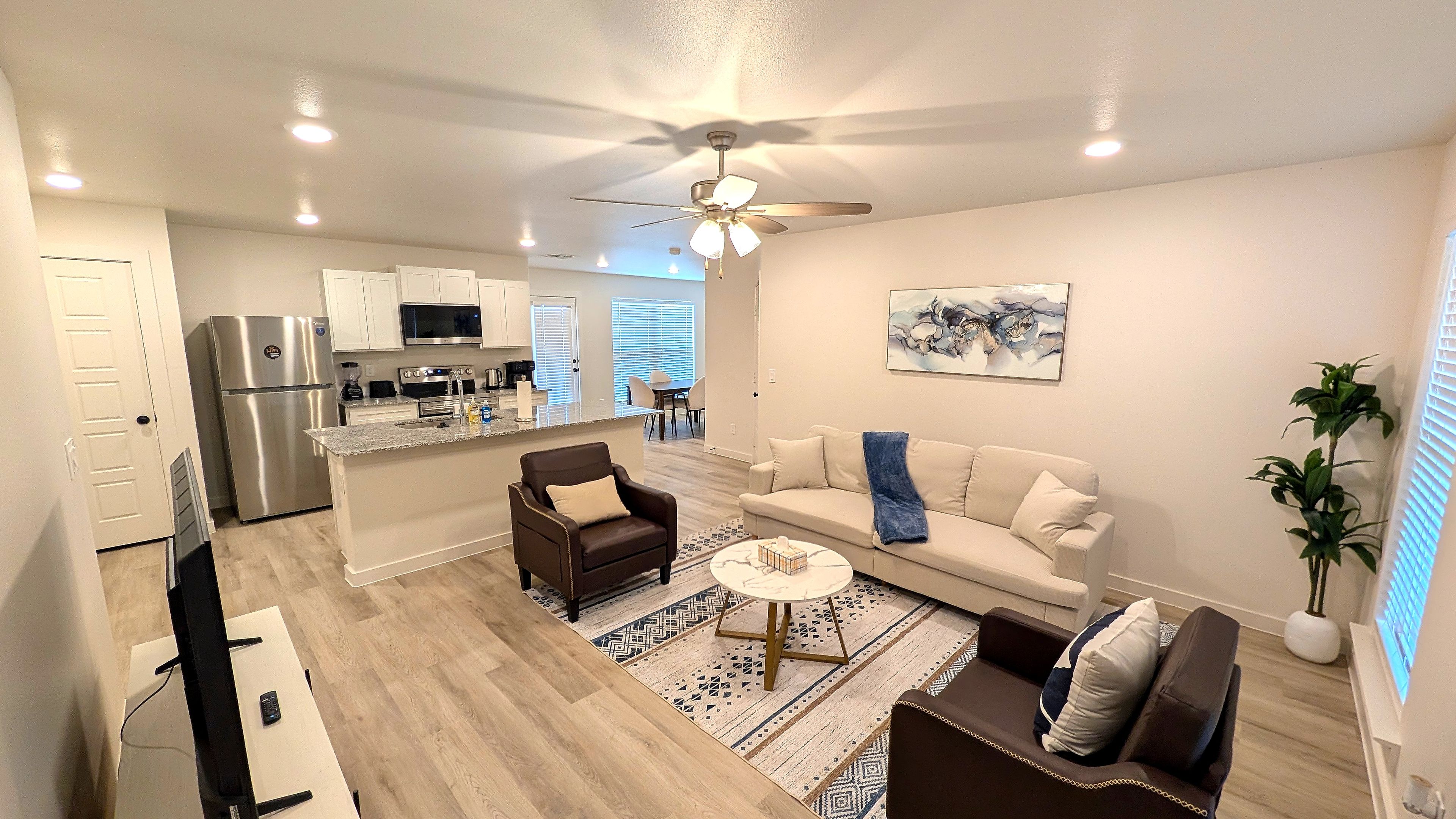 Un salon moderne avec un canapé, des fauteuils, une table basse et un ventilateur de plafond.