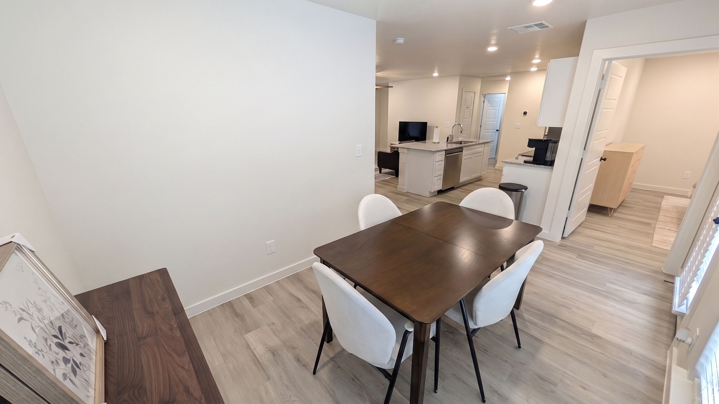 Une cuisine moderne avec des meubles blancs, un îlot central et un coin repas comprenant une table en bois foncé et des chaises blanches.