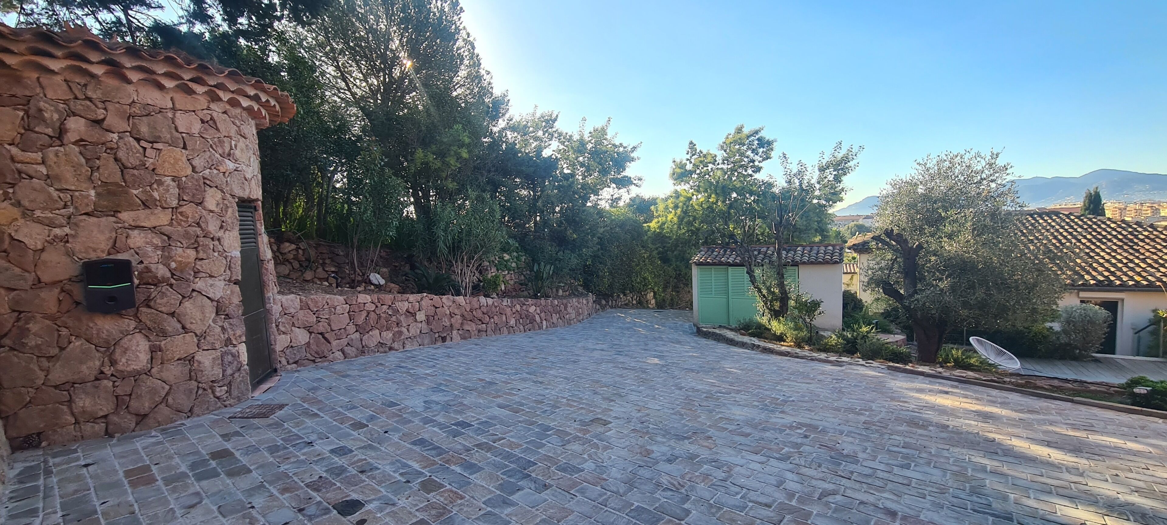 A paved courtyard with stone walls, a small green shed, and a satellite dish.