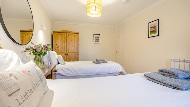 Een hotelkamer met twee bedden, een houten garderobe, een spiegel, een lijst met een afbeelding en een vaas met bloemen.