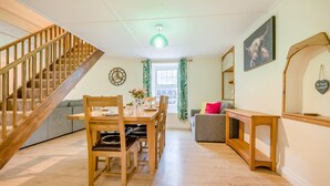 Een modern interieur met een houten trap, een eethoek met een tafel gedekt voor twee personen, een bank en een spiegel.