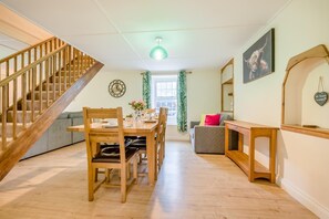 A modern interior with a wooden staircase, a dining area with a table set for two, a sofa, and a mirror. - 2 Bed in St. Issey (oc-m31992) (Tredinnick)