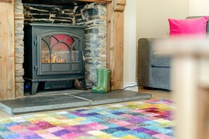 A cozy room with a stone fireplace, a colorful rug, and a grey sofa. - 2 Bed in St. Issey (oc-m31992) (Tredinnick)