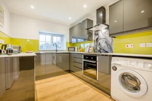 A modern kitchen with a built-in washing machine, a microwave, and a stainless steel range hood. - 2 Bed in St. Issey (oc-c31993) (Tredinnick)