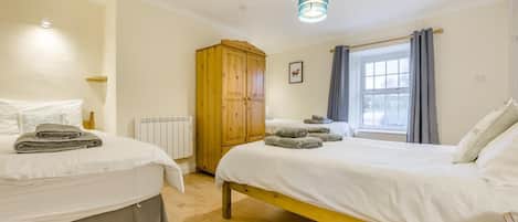 A bedroom with two beds, a wooden wardrobe, a radiator, and a window with curtains.