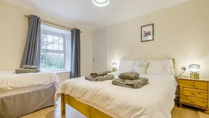 Et soveværelse med seng, sengebord, lampe, et vindue med gardiner og en lampe på væggen.