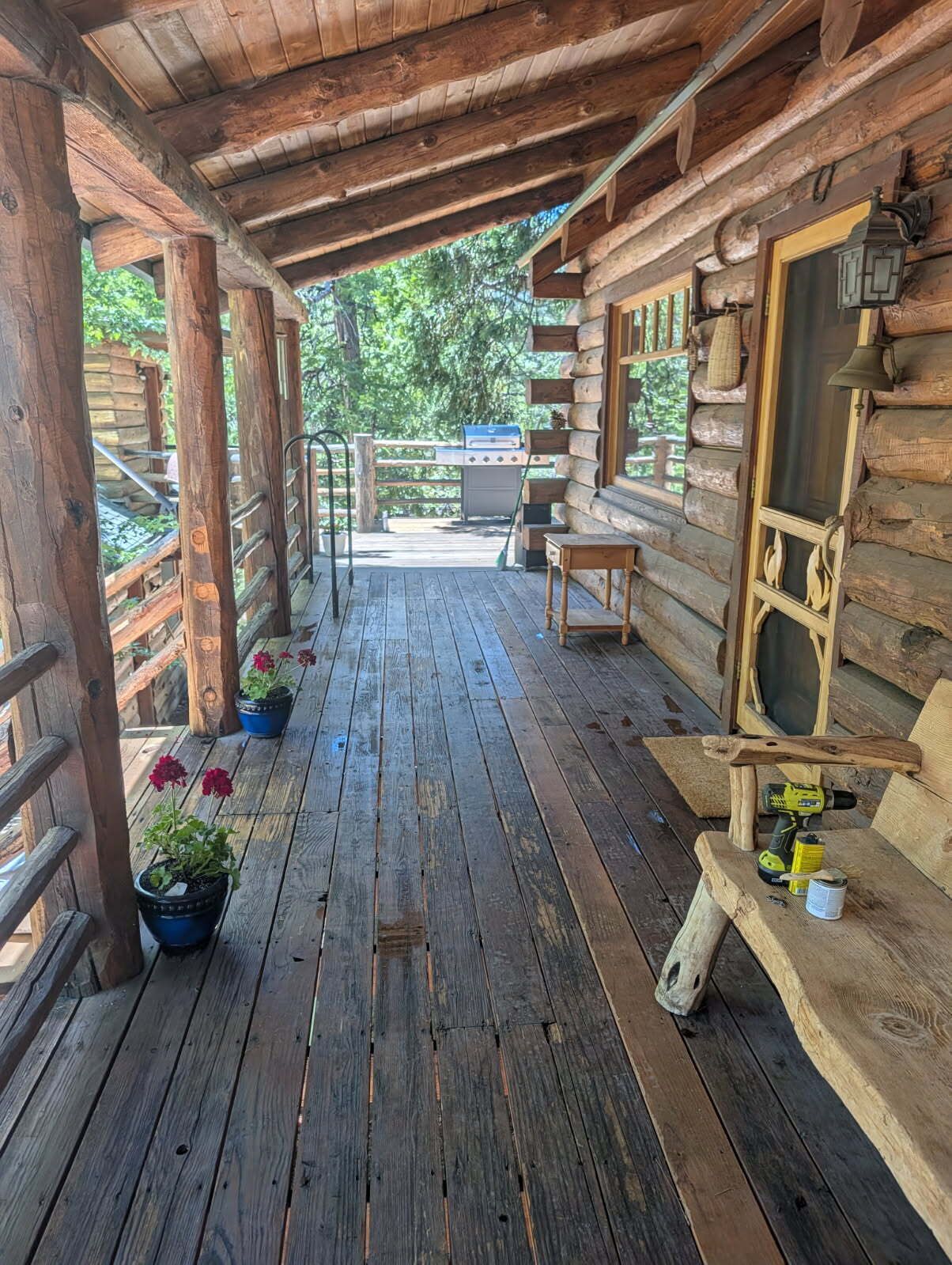A wooden deck with a grill, potted plants, and a bench.