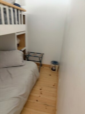 Una habitación pequeña con una cama individual superpuesta, una mesita y un cubo de basura.