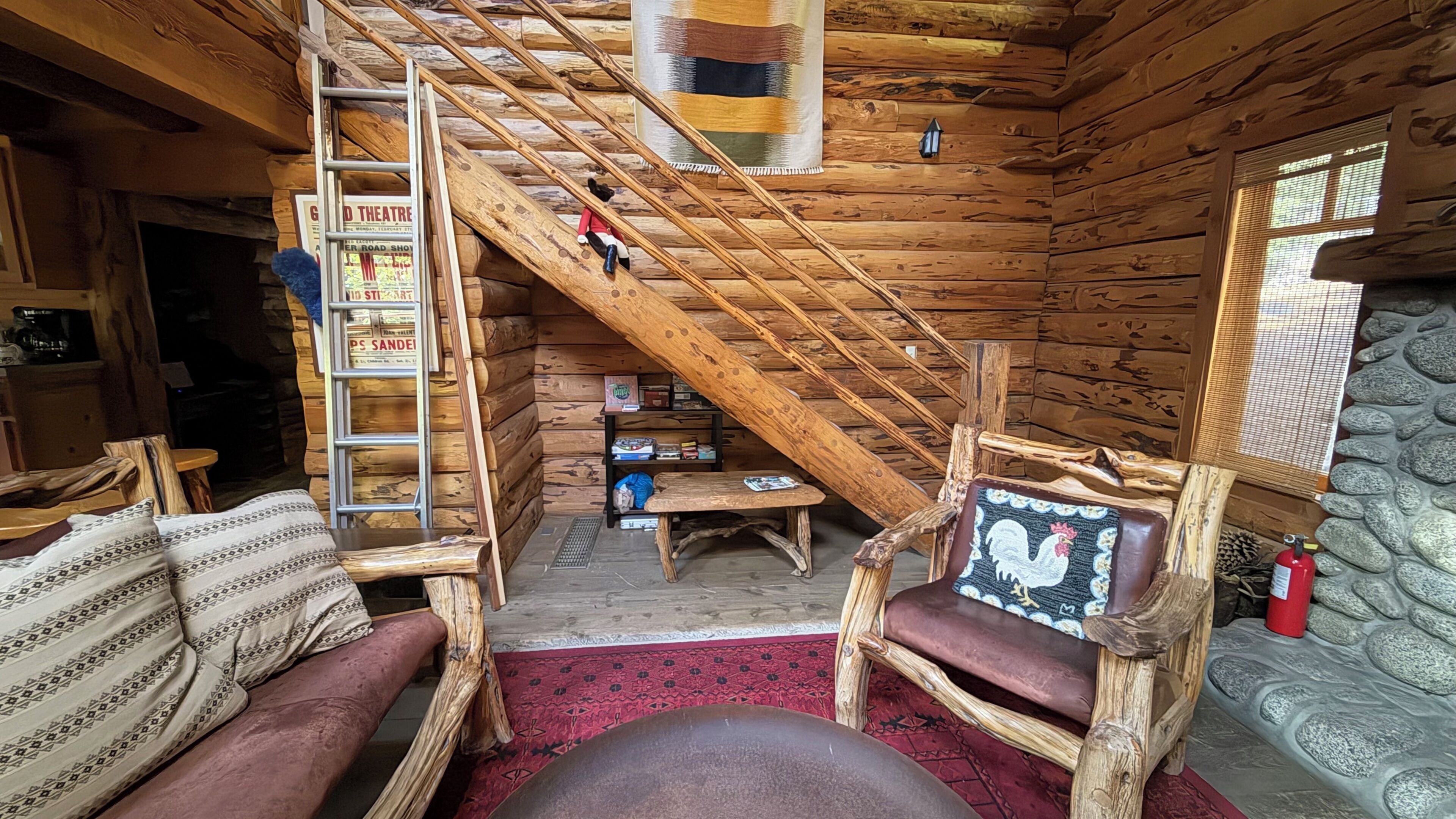 A log cabin interior with a wooden staircase, a loft area, and a cozy seating arrangement.
