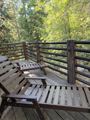 Eine Holzterrasse mit Bänken und einem Geländer, umgeben von Bäumen.