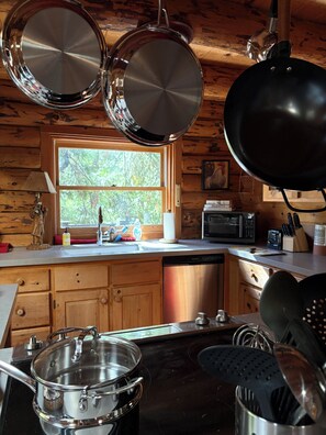 Una cocina con armarios de madera, una ventana con vistas a árboles, un microondas y varios utensilios de cocina.