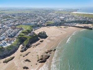 An aerial view of a coastal town with a sandy beach, rocky outcrops, and a mix of residential and commercial buildings. - 3 Bed in Newquay (oc-o32258) (Newquay)
