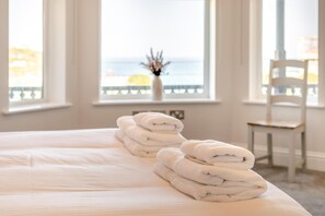 A hotel room with a bed, a chair, and a view of the sea through large windows. - 3 Bed in Newquay (oc-o32258) (Newquay)